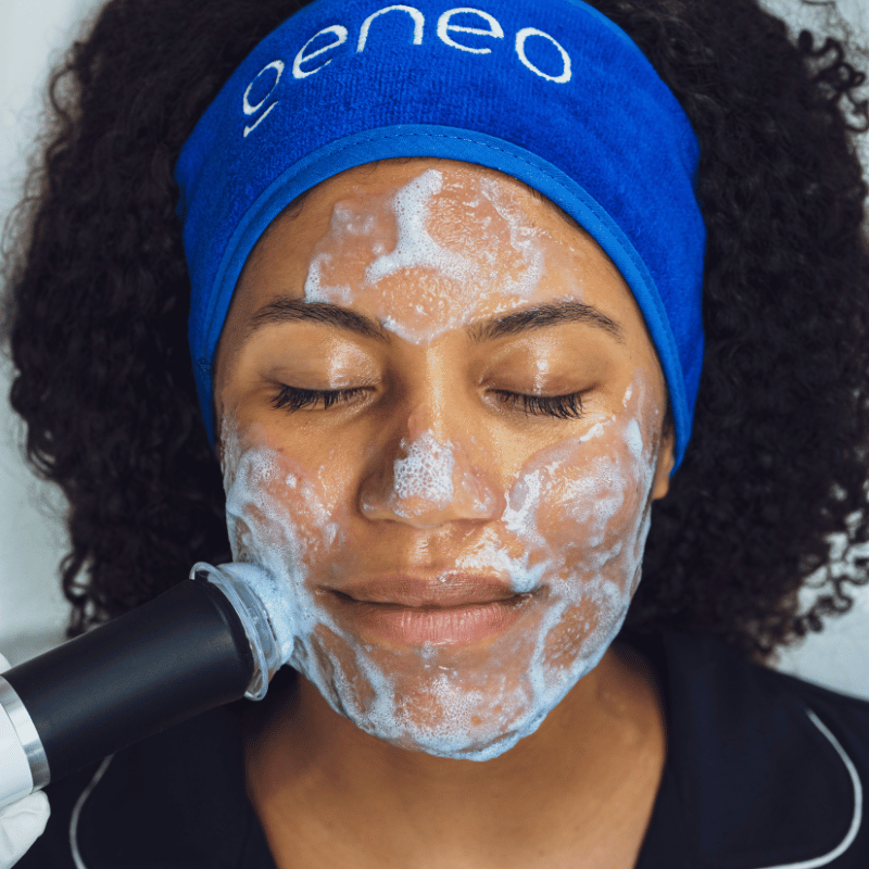 Woman receiving Geneo Hydrate facial treatment, wearing blue headband