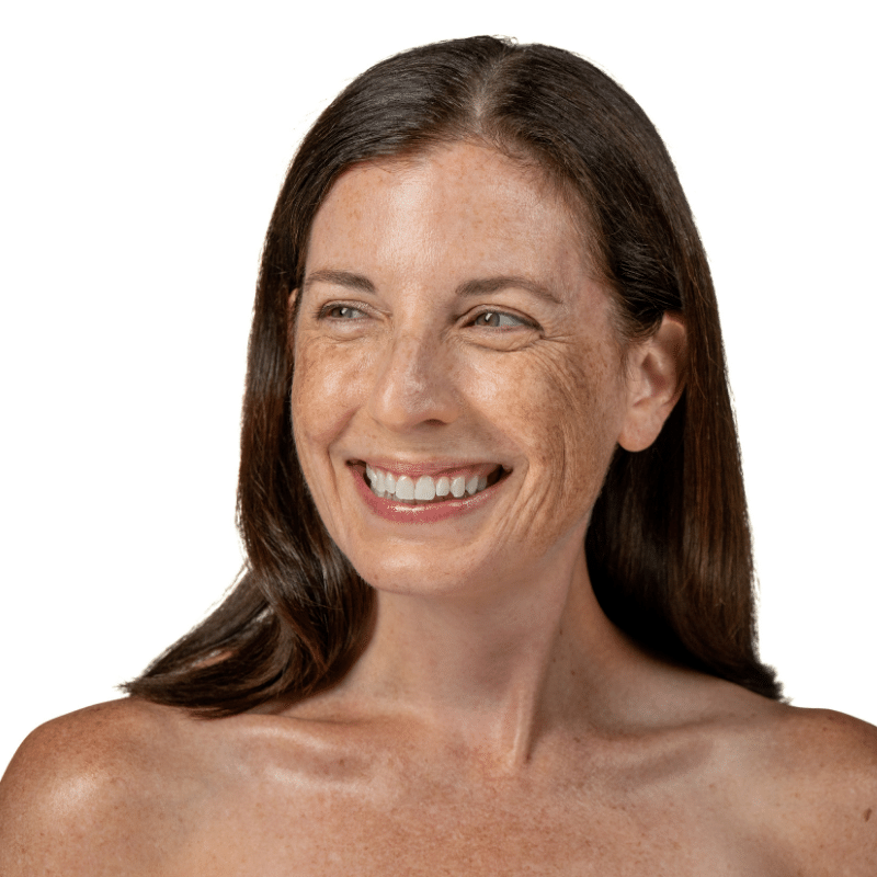 Older woman with dark, straight hair and glowing, freckled skin smiling and looking off to the side