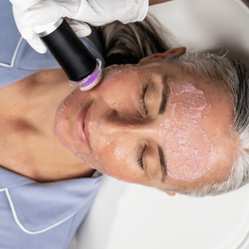 Woman receiving Geneo Revive facial treatment, older woman with grey hair