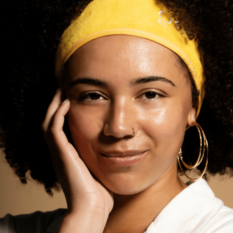 Woman with beautiful, glowing skin wearing yellow headband with hand on face